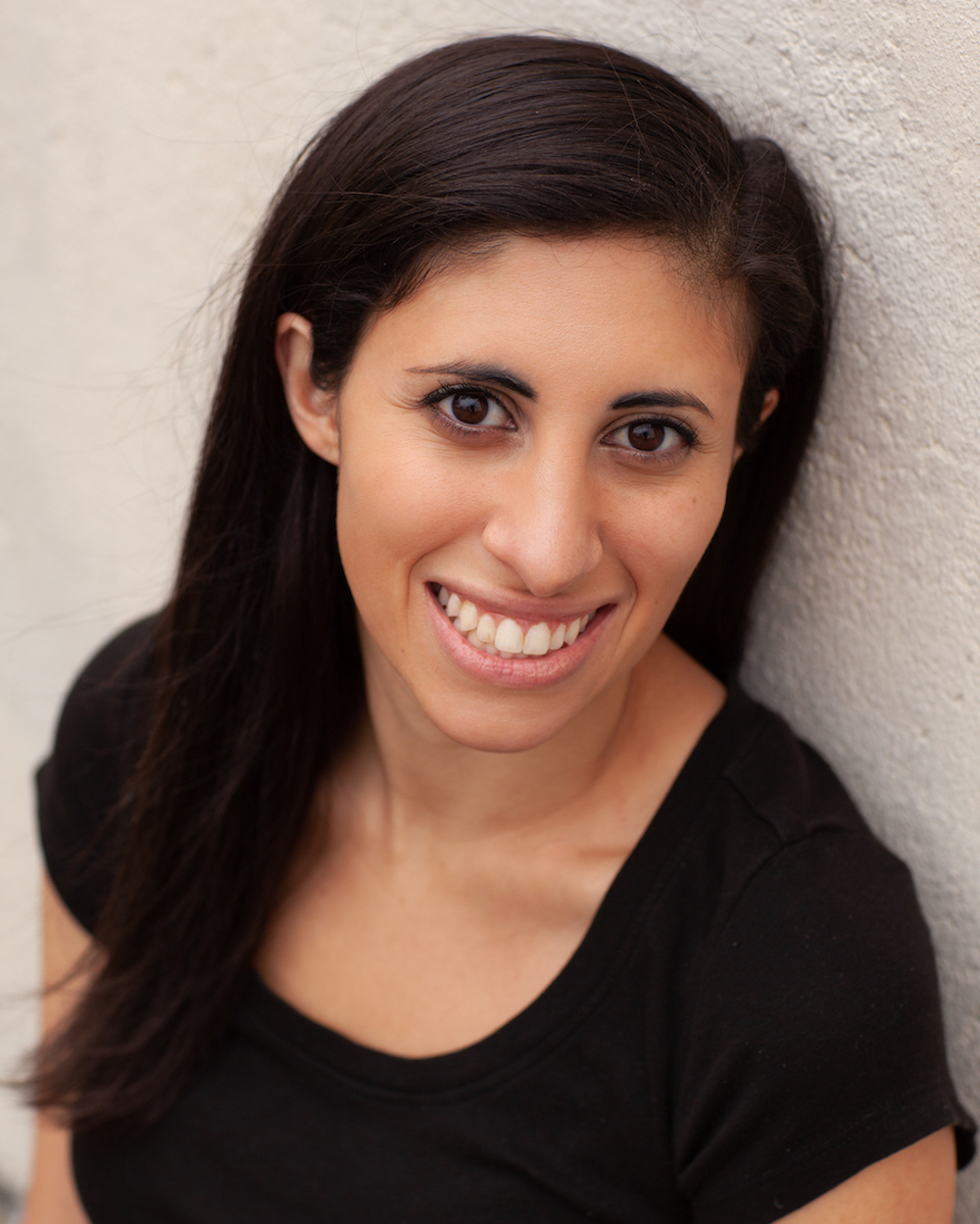 Leila, an Arab woman smiles at the camera wearing a black short sleeved shirt 