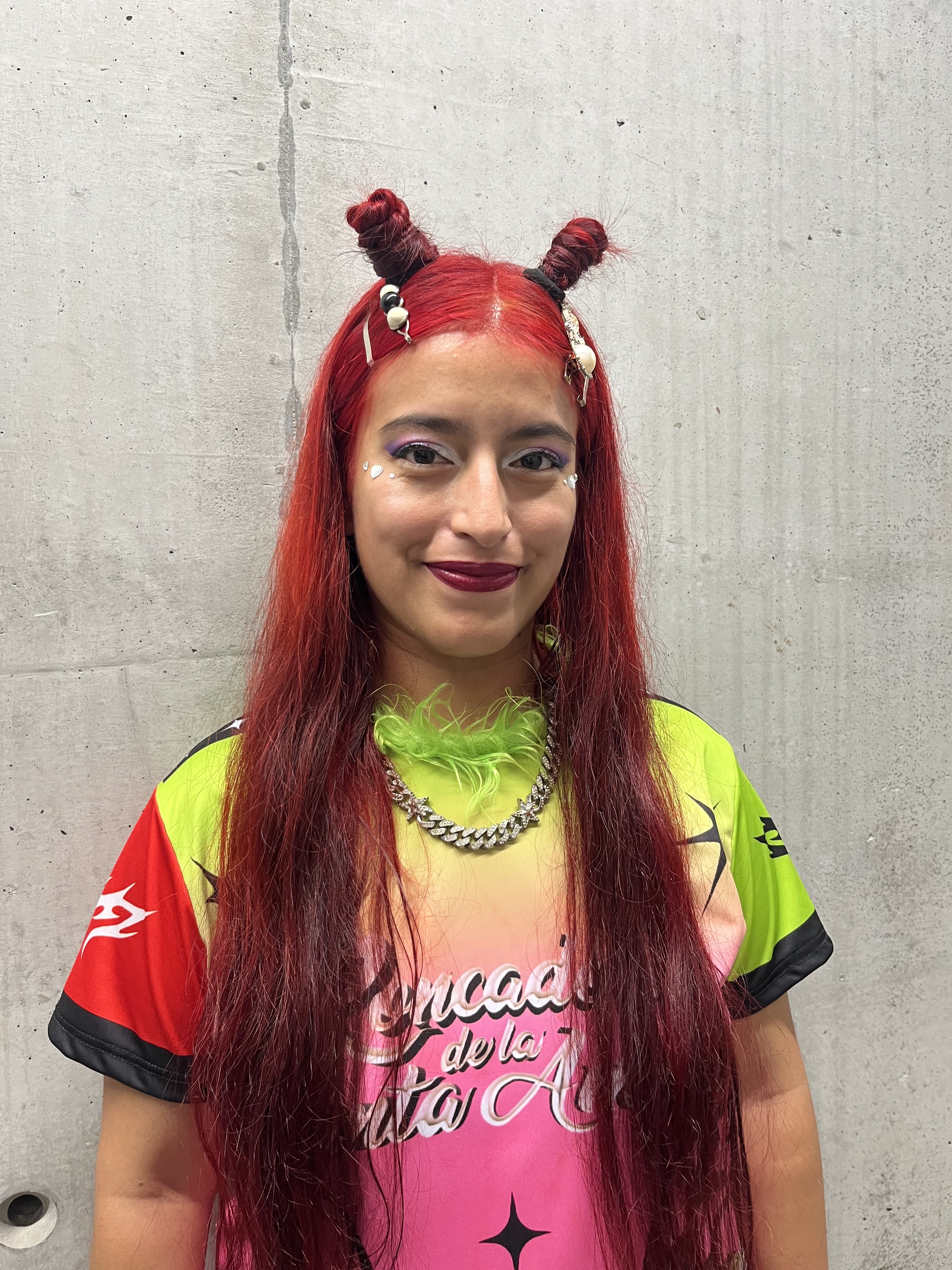 Patricia, an urban light brown afroindigenous non-binary person with long red hair and a colorful t-shirt.